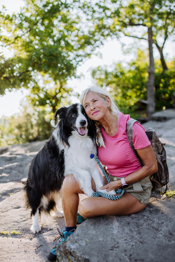 Senior woman resting and stroking her dog during walking in a forest.