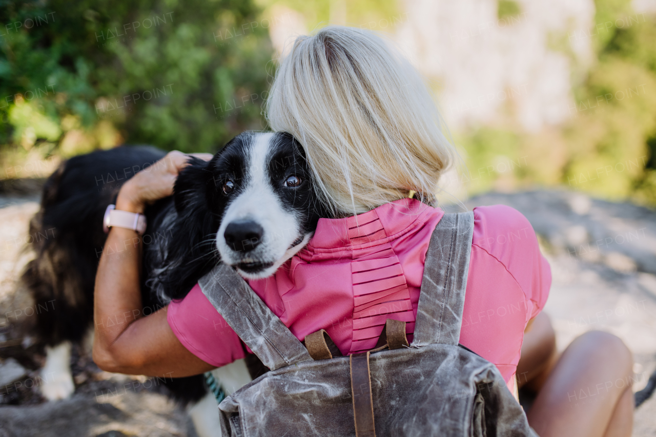 Senior woman resting and hugging her dog during walking in a forest.