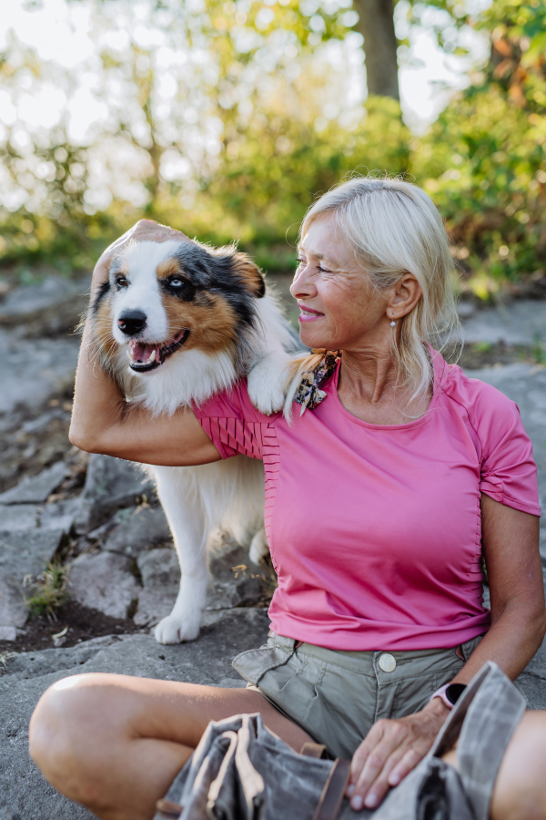 Senior woman resting and stroking her dog during walking in a forest.