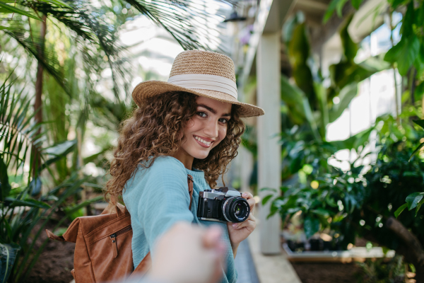 Portrait of young beautiful woman with camera in botanical garden.