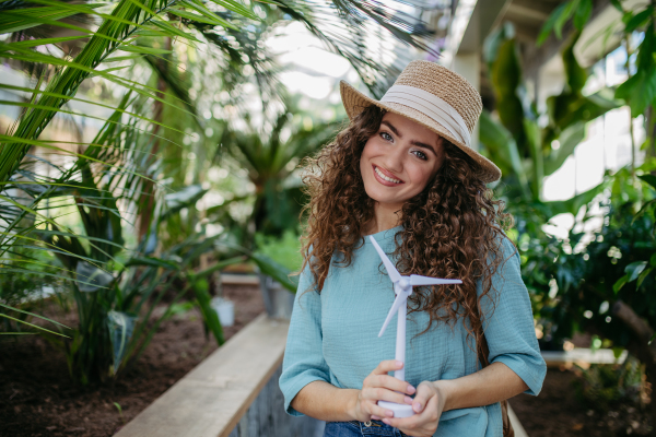 Young woman in a botanical garden holding model of wind turbine, concept of green energy.