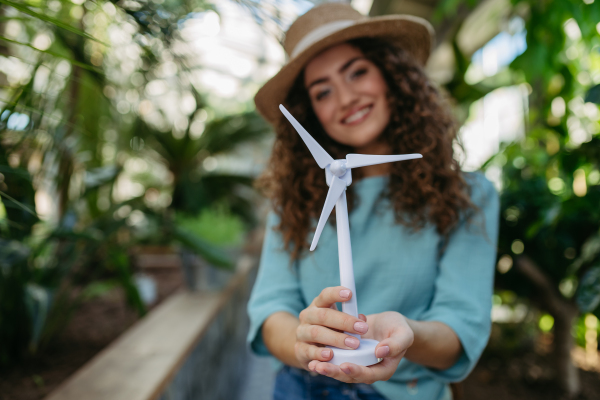 Young woman in a botanical garden holding model of wind turbine, concept of green energy.