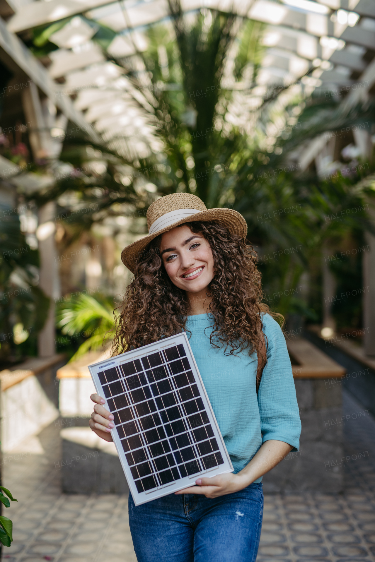 Young woman in a botanical garden holding solar panel, concept of green energy.