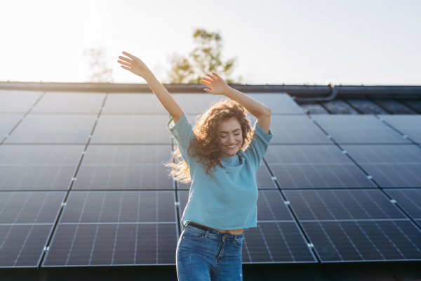 Portrait of young excited woman, owner on roof with solar panels.