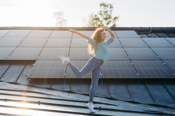 Portrait of young excited woman, owner on roof with solar panels.