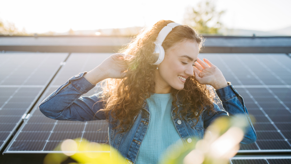 Portrait of young excited woman, owner on roof with solar panels, listening music.