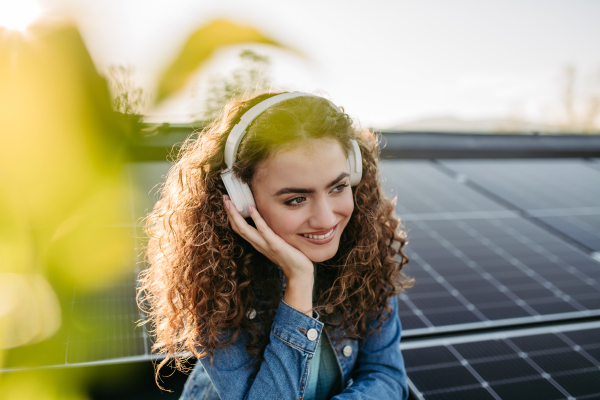 Portrait of young excited woman, owner on roof with solar panels, listening music.