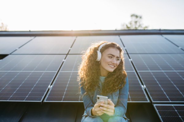 Portrait of young excited woman, owner on roof with solar panels, listening music.