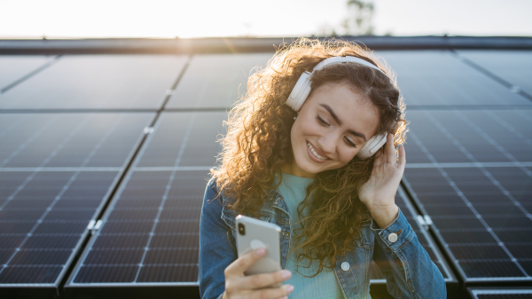 Portrait of young excited woman, owner on roof with solar panels, listening music.