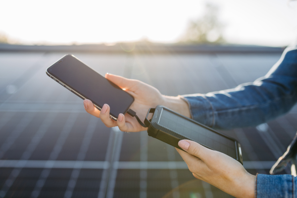 Close up of a woman charging her phone with solar charger on the roof with photovoltaics panels.