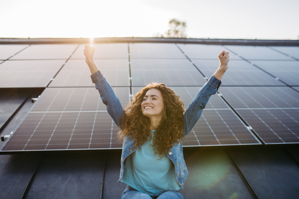 Portrait of young excited woman, owner on roof with solar panels.