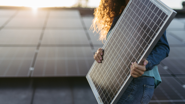 Close up of a woman holding solar panel on the roof with photovoltaics panels.