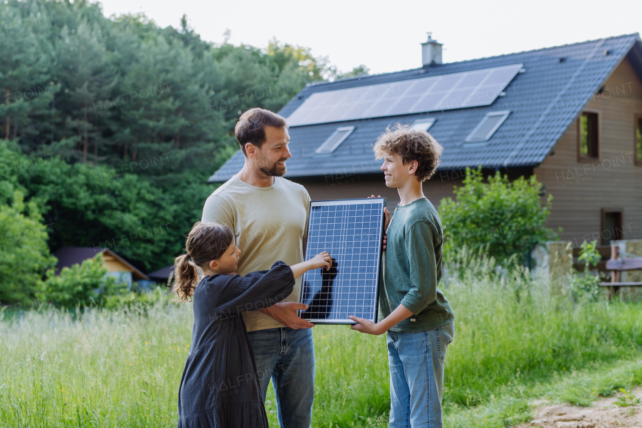 Father and his children standing in front of their house with photovoltaics on the roof.