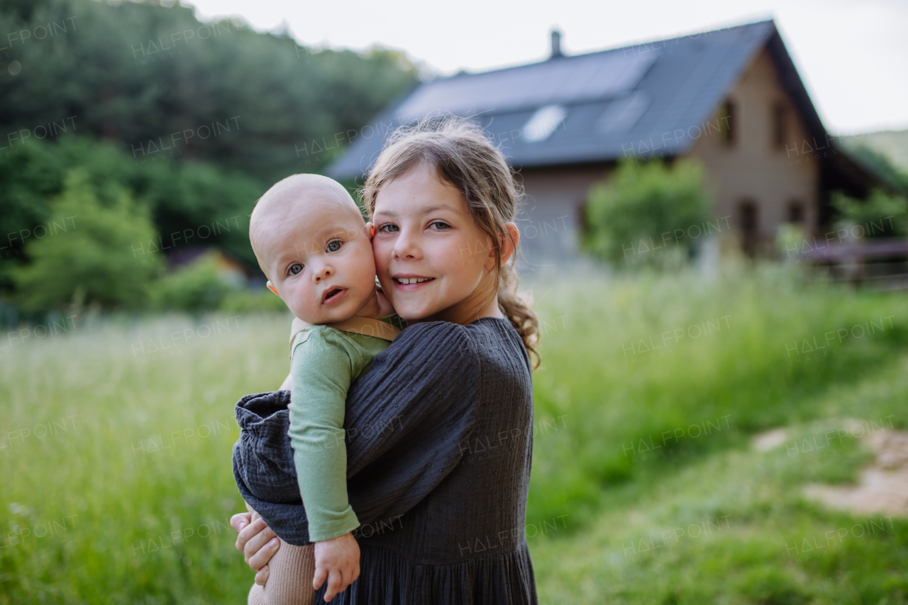 Girl standing with her little brother in front of the house with solar panels.