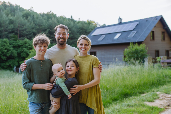 Happy family near their house with a solar panels. Alternative energy, saving resources and sustainable lifestyle concept.