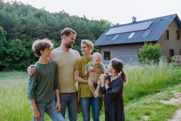 Happy family near their house with a solar panels. Alternative energy, saving resources and sustainable lifestyle concept.