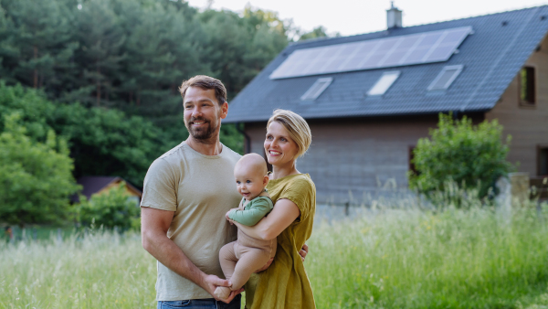 Happy family near their house with a solar panels. Alternative energy, saving resources and sustainable lifestyle concept.