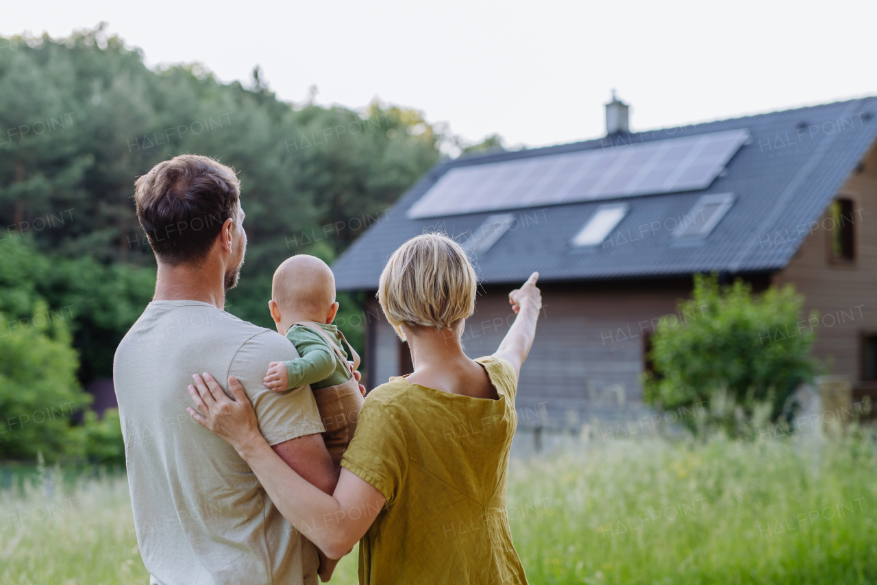 Rear view of family near their house with a solar panels. Alternative energy, saving resources and sustainable lifestyle concept.