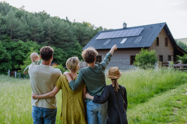 Rear view of family near their house with a solar panels. Alternative energy, saving resources and sustainable lifestyle concept.