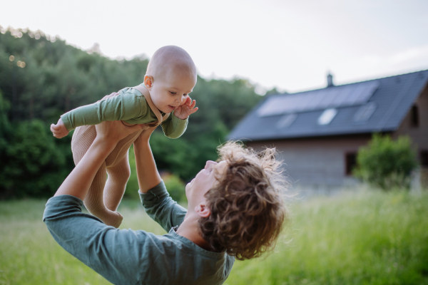 Boy playing with his little brother in front of the house with solar panels.