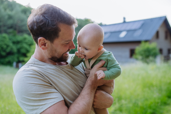 Happy father with baby boy standing in front of their house with solar panels.