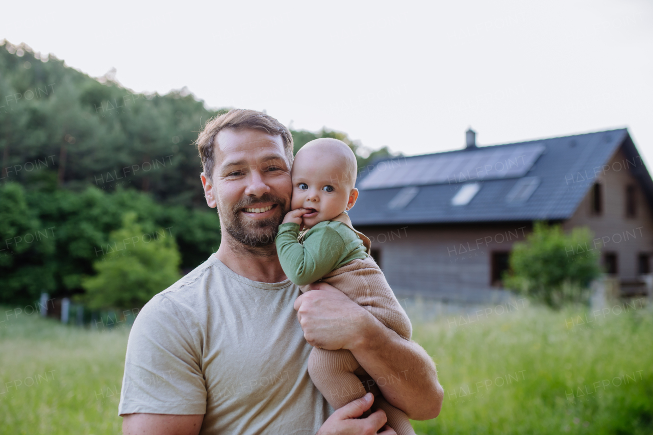 Happy father with baby boy standing in front of their house with solar panels.