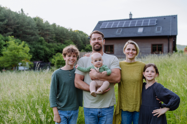 Happy family near their house with a solar panels. Alternative energy, saving resources and sustainable lifestyle concept.