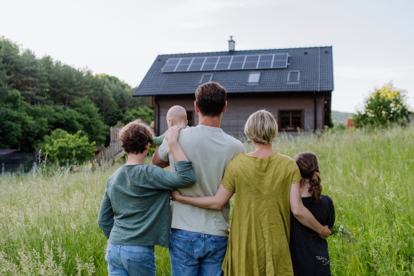 Rear view of family near their house with a solar panels. Alternative energy, saving resources and sustainable lifestyle concept.