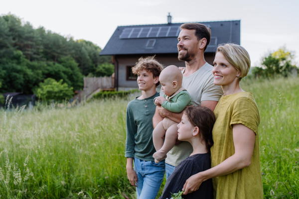 Happy family near their house with a solar panels. Alternative energy, saving resources and sustainable lifestyle concept.