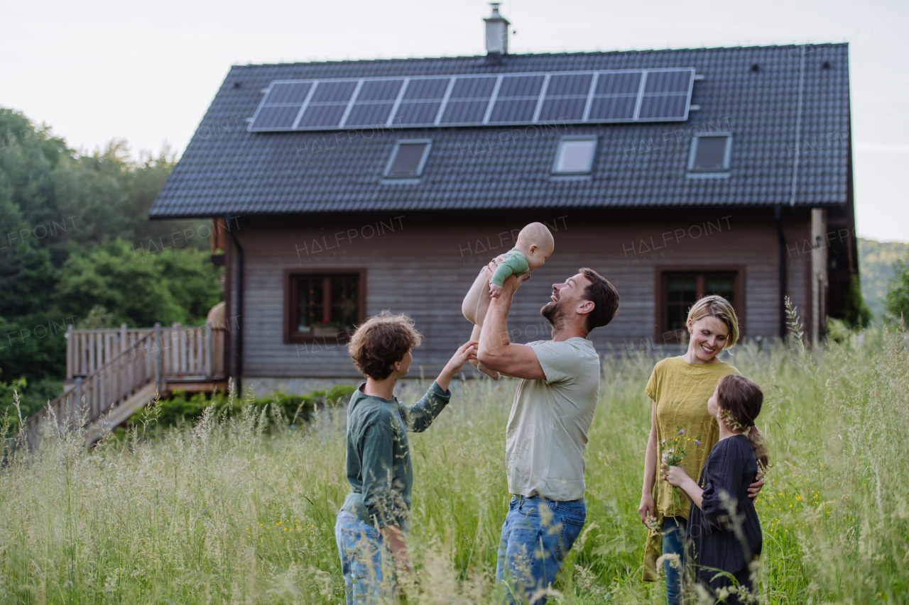 Happy family near their house with a solar panels. Alternative energy, saving resources and sustainable lifestyle concept.