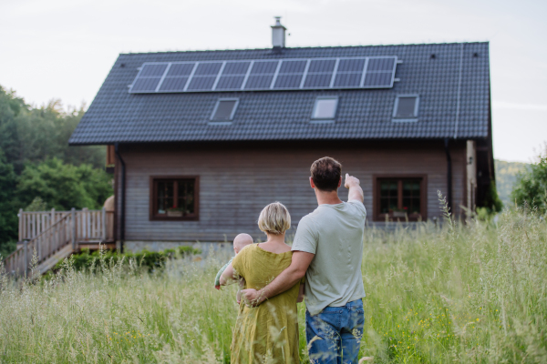 Rear view of family near their house with a solar panels. Alternative energy, saving resources and sustainable lifestyle concept.