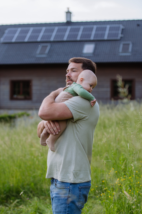 Happy father with baby boy standing in front of their house with solar panels.