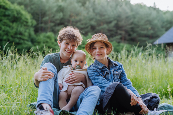 Portrait of three children, siblings sitting in a grass, having fun together.