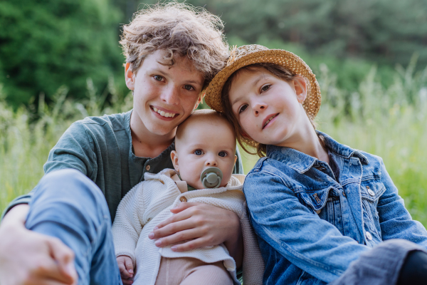 Portrait of three children, siblings sitting in a grass, having fun together.