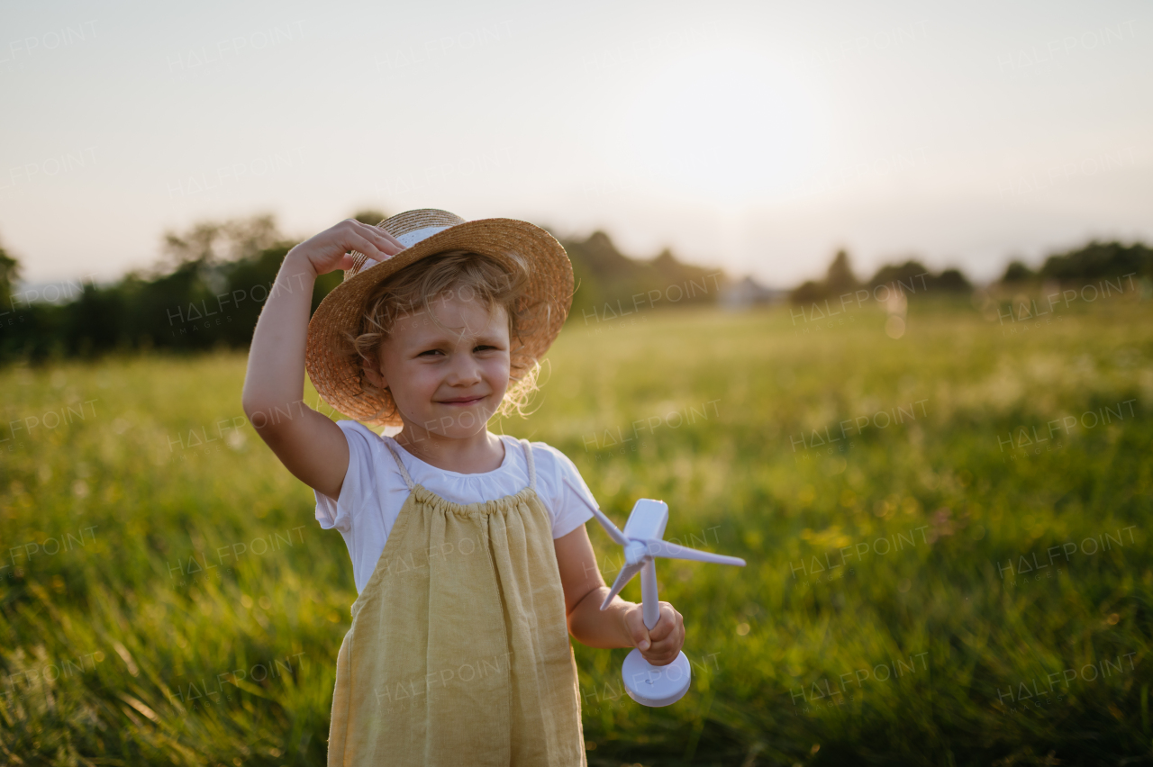 Little girl with model of wind turbine, standing in the middle of meadow Concept of renewable resources. Importance of alternative energy sources and long-term sustainability for future generations