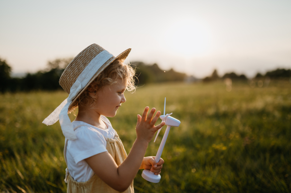 Little girl with model of wind turbine, standing in the middle of meadow Concept of renewable resources. Importance of alternative energy sources and long-term sustainability for future generations