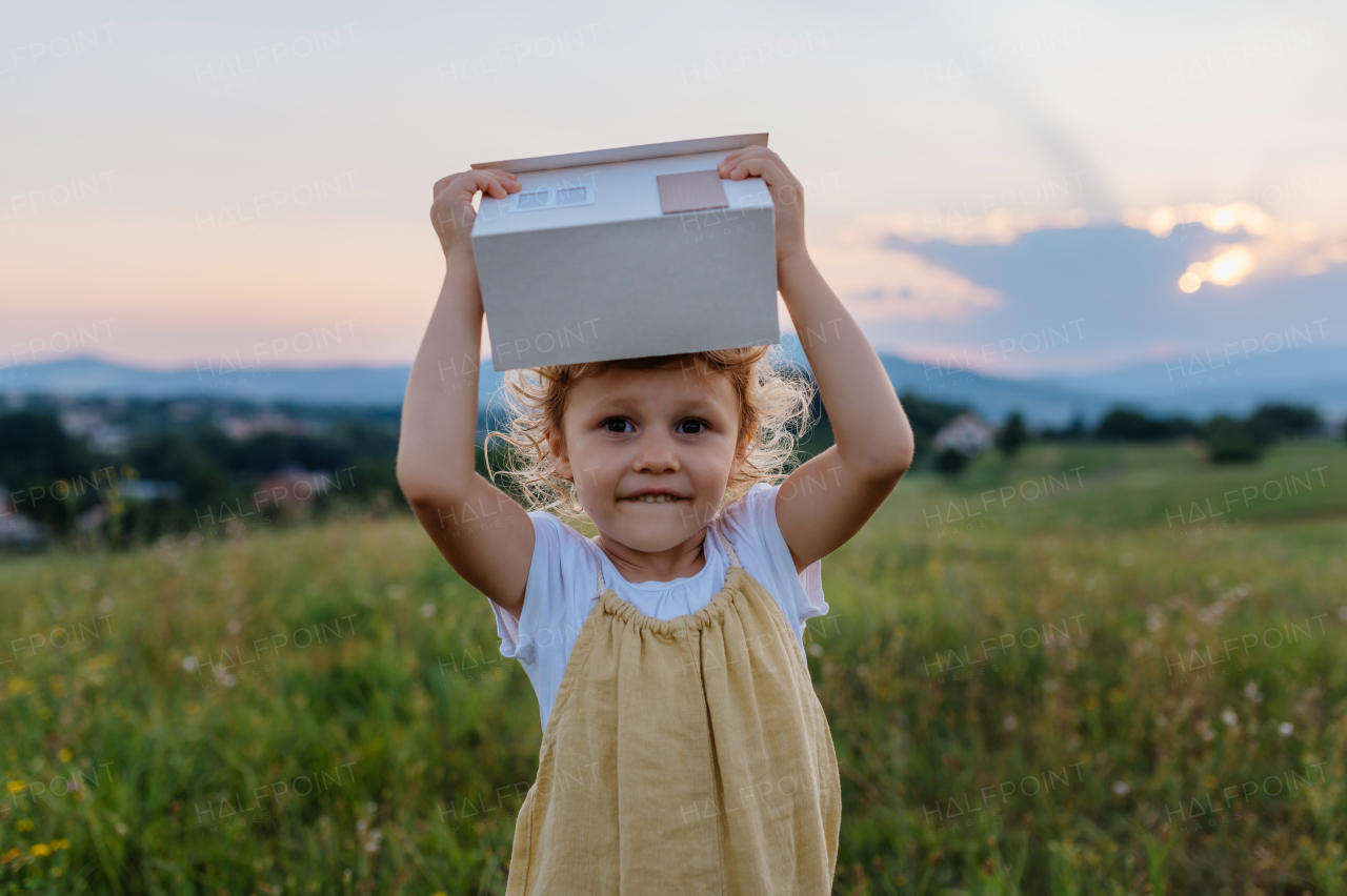 Little girl with model house with installed of solar panels, standing in the middle of meadow. Concept of alternative energy, saving resources and sustainable lifestyle concept. . Importance of alternative energy sources and long-term sustainability for future generations