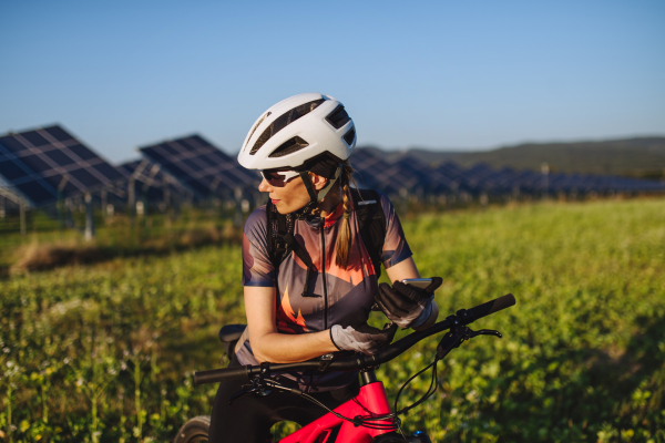 Portrait of a beautiful cyclist standing in front of solar panels at a solar farm during a summer bike tour in nature. A solar farm as solution for more sustainable energy future.