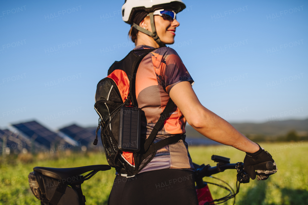 Portrait of a beautiful cyclist standing in front of solar panels at a solar farm during a summer bike tour in nature. A solar farm as solution for more sustainable energy future.