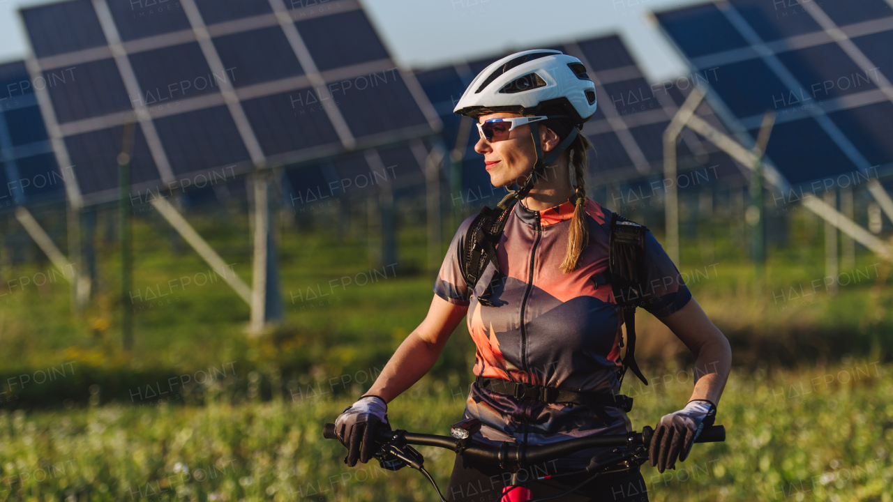 Portrait of a beautiful cyclist standing in front of solar panels at a solar farm during a summer bike tour in nature. A solar farm as solution for more sustainable energy future.