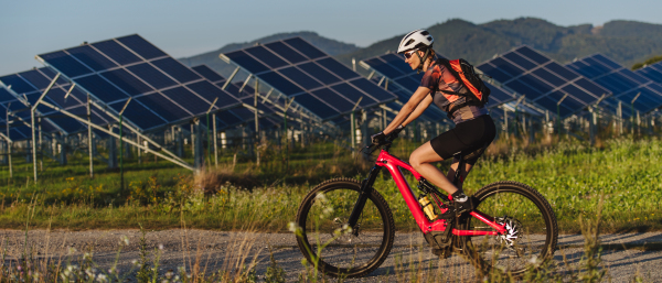 Side view of a beautiful cyclist riding in front of solar panels at a solar farm during a summer bike tour in nature. A solar farm as solution for more sustainable energy future. Sport, ecology, nature banner with copy space.