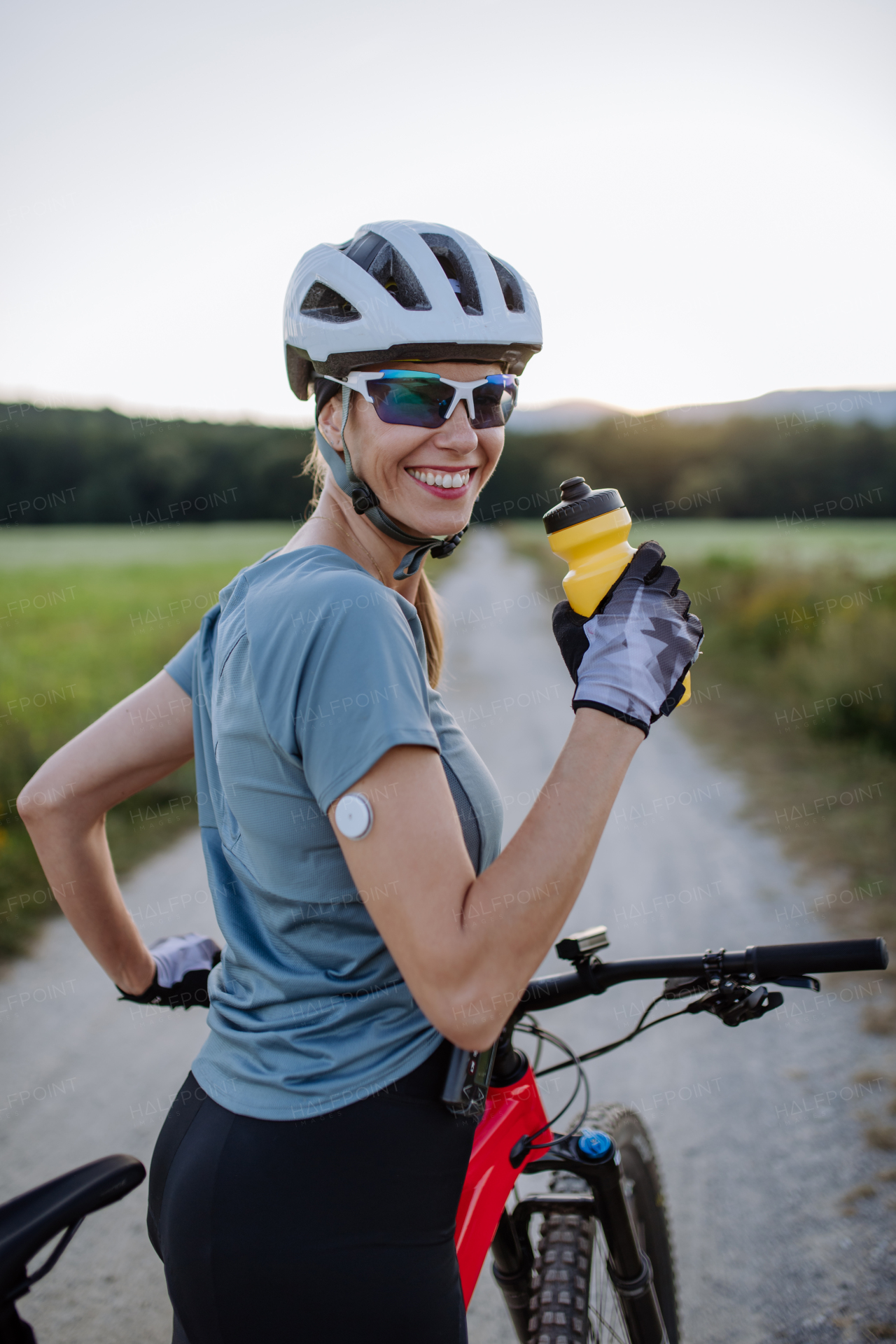 Diabetic cyclist with a continuous glucose monitor on her arm drinking water during her bike tour to manage her diabetes while exercising. Concept of exercise and diabetes.