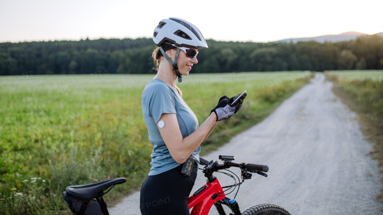 Diabetic cyclist with continuous glucose monitor checking on smartphone smartphone her blood sugar levels in real time. Concept of exercise and diabetes.