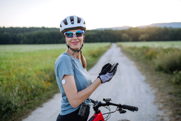 Diabetic cyclist with continuous glucose monitor checking on smartphone smartphone her blood sugar levels in real time. Concept of exercise and diabetes.