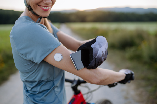 Diabetic cyclist connecting continuous glucose monitor with her smartphone to monitor her blood sugar levels in real time. Concept of exercise and diabetes.