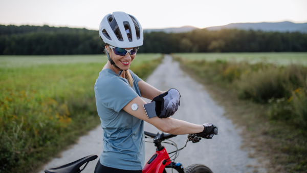 Diabetic cyclist connecting continuous glucose monitor with her smartphone to monitor her blood sugar levels in real time. Concept of exercise and diabetes.