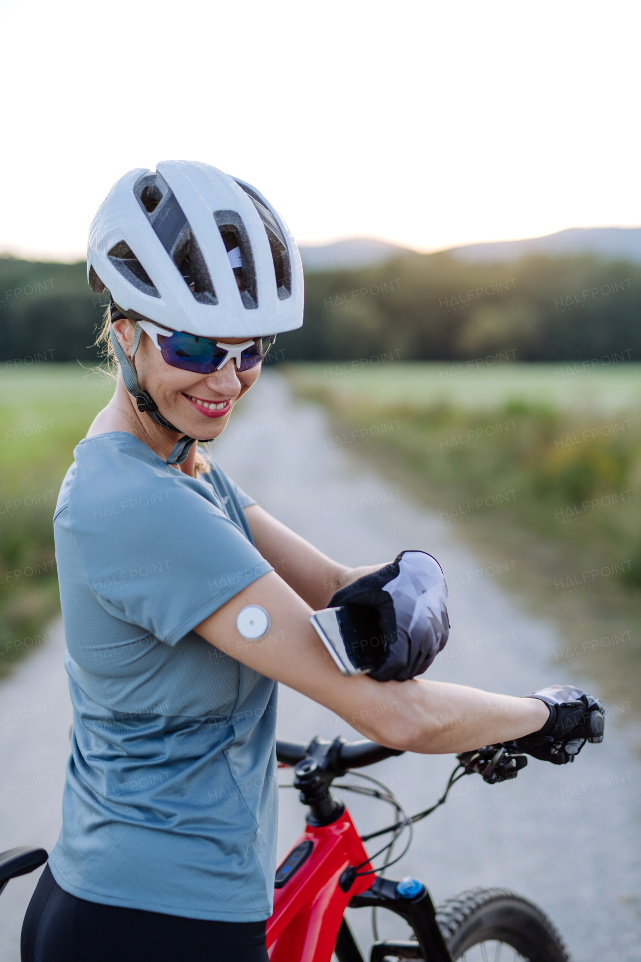 Diabetic cyclist with continuous glucose monitor checking on smartphone smartphone her blood sugar levels in real time. Concept of exercise and diabetes.