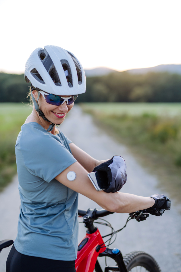 Diabetic cyclist with continuous glucose monitor checking on smartphone smartphone her blood sugar levels in real time. Concept of exercise and diabetes.