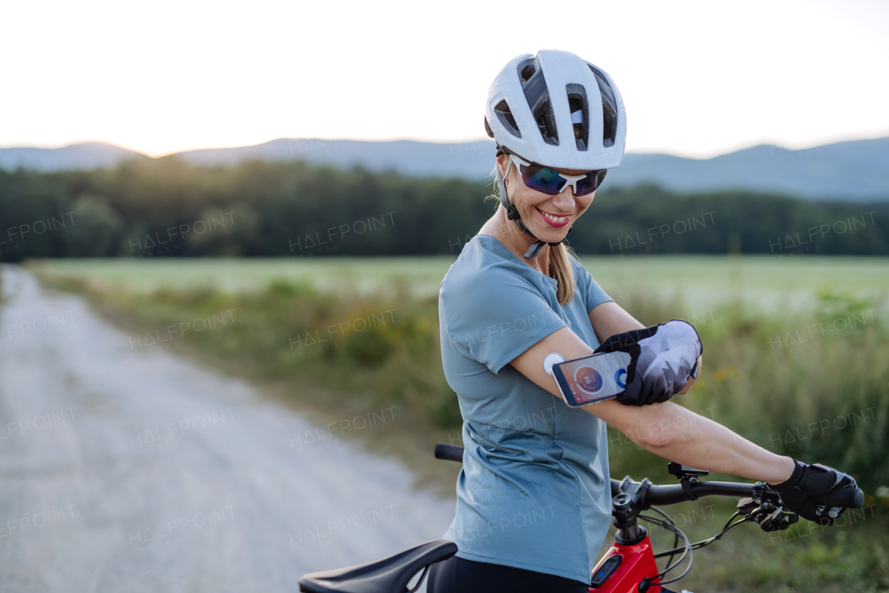 Diabetic cyclist connecting continuous glucose monitor with her smartphone to monitor her blood sugar levels in real time. Concept of exercise and diabetes.