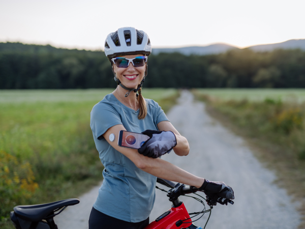 Diabetic cyclist connecting continuous glucose monitor with her smartphone to monitor her blood sugar levels in real time. Concept of exercise and diabetes.